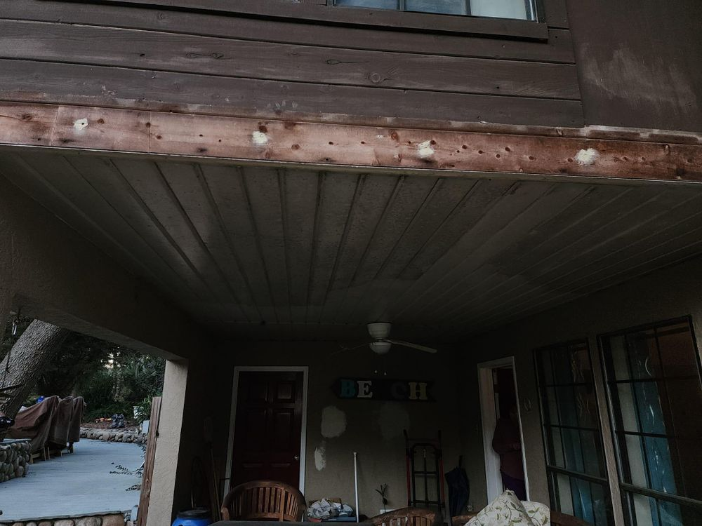 Exterior porch with brown wood siding showing areas of damage and repair.