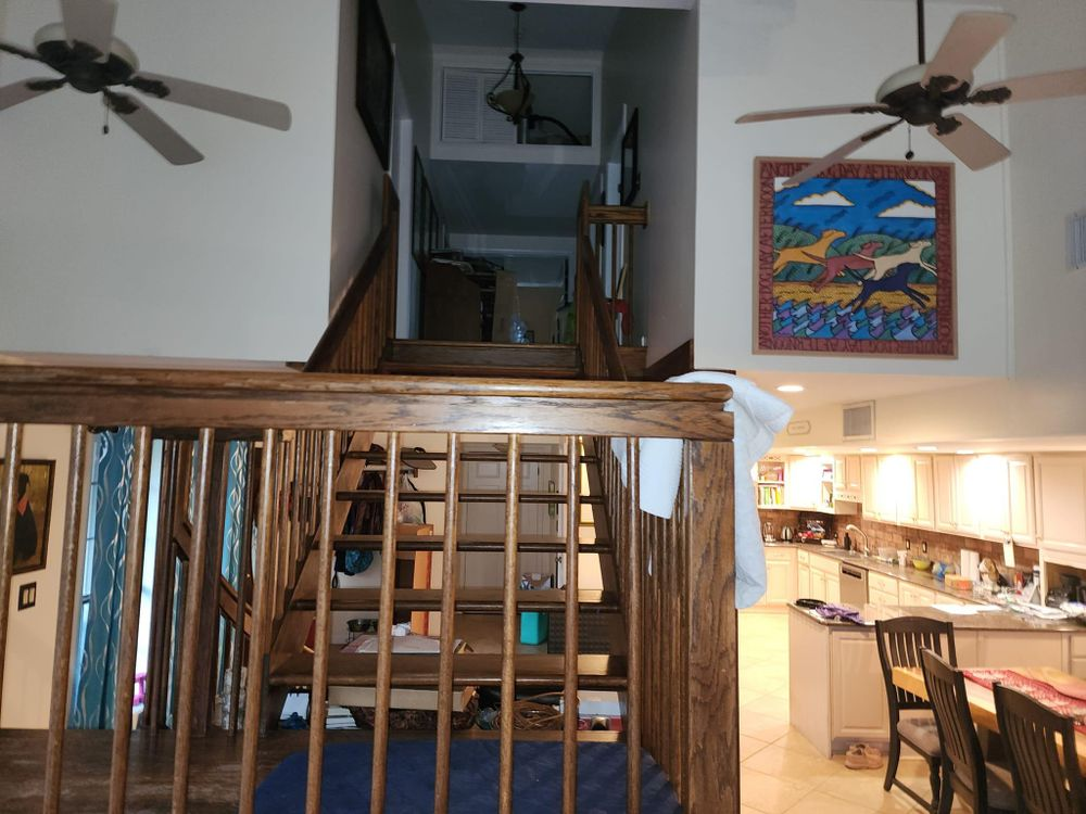 Staircase leads to an upper level with a kitchen visible in the background. Ceiling fans and art on the walls.