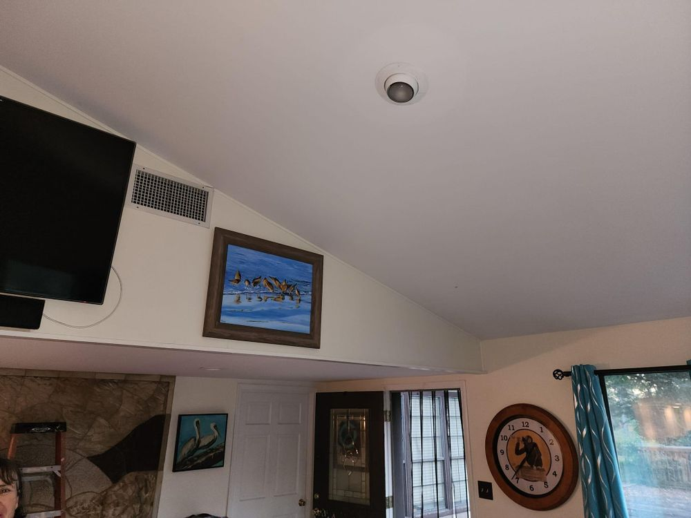 A living room with a high, angled ceiling, art, a television, and a round clock on the wall.