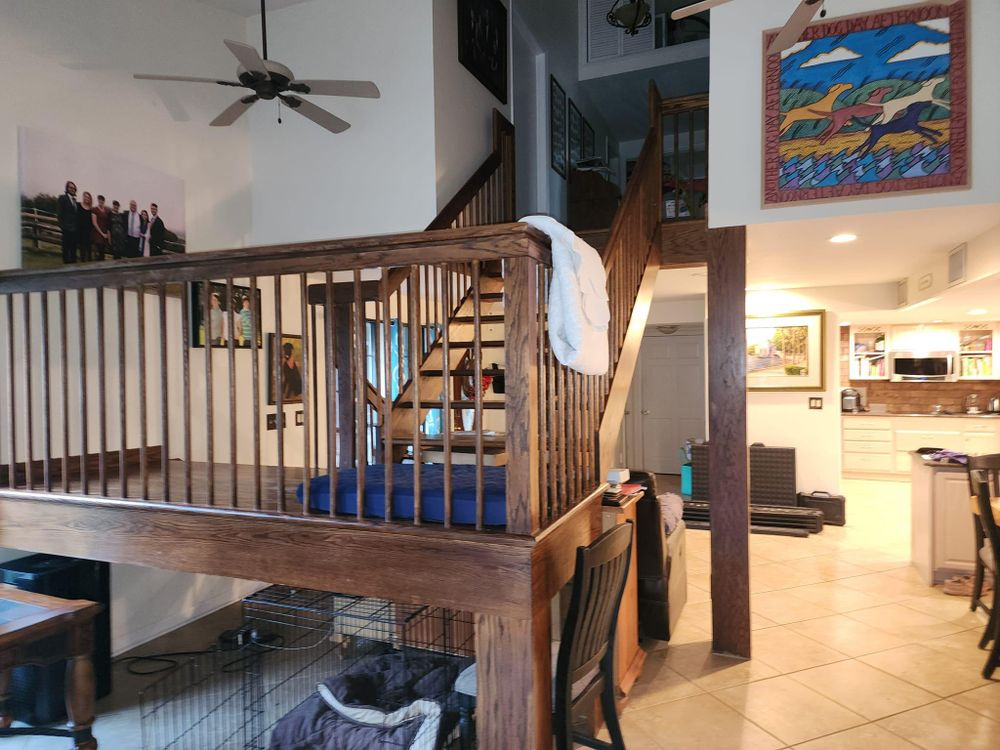 Wooden staircase and loft overlooking a kitchen, a rug with a dog bed, and colorful artwork.
