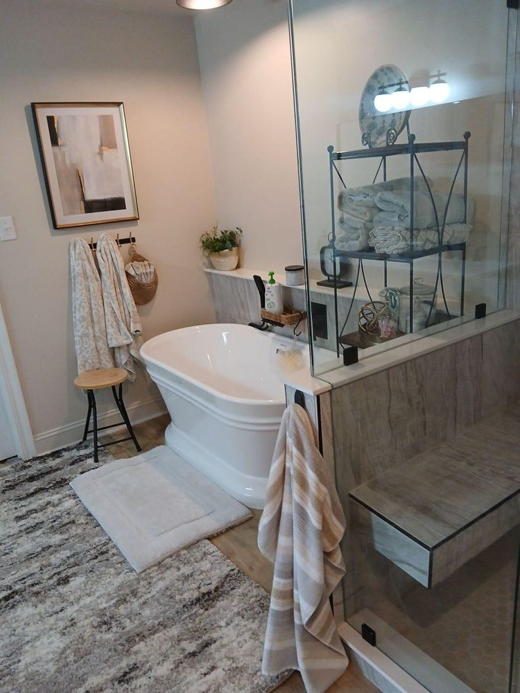 Bathroom with a white tub, shower with glass door, gray and white rug, towels.