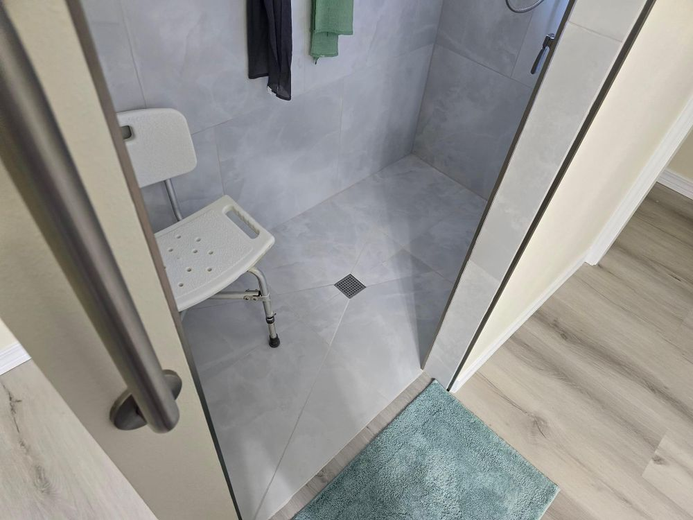 Shower with accessible seat and grab bar. Light gray tiles, teal mat.