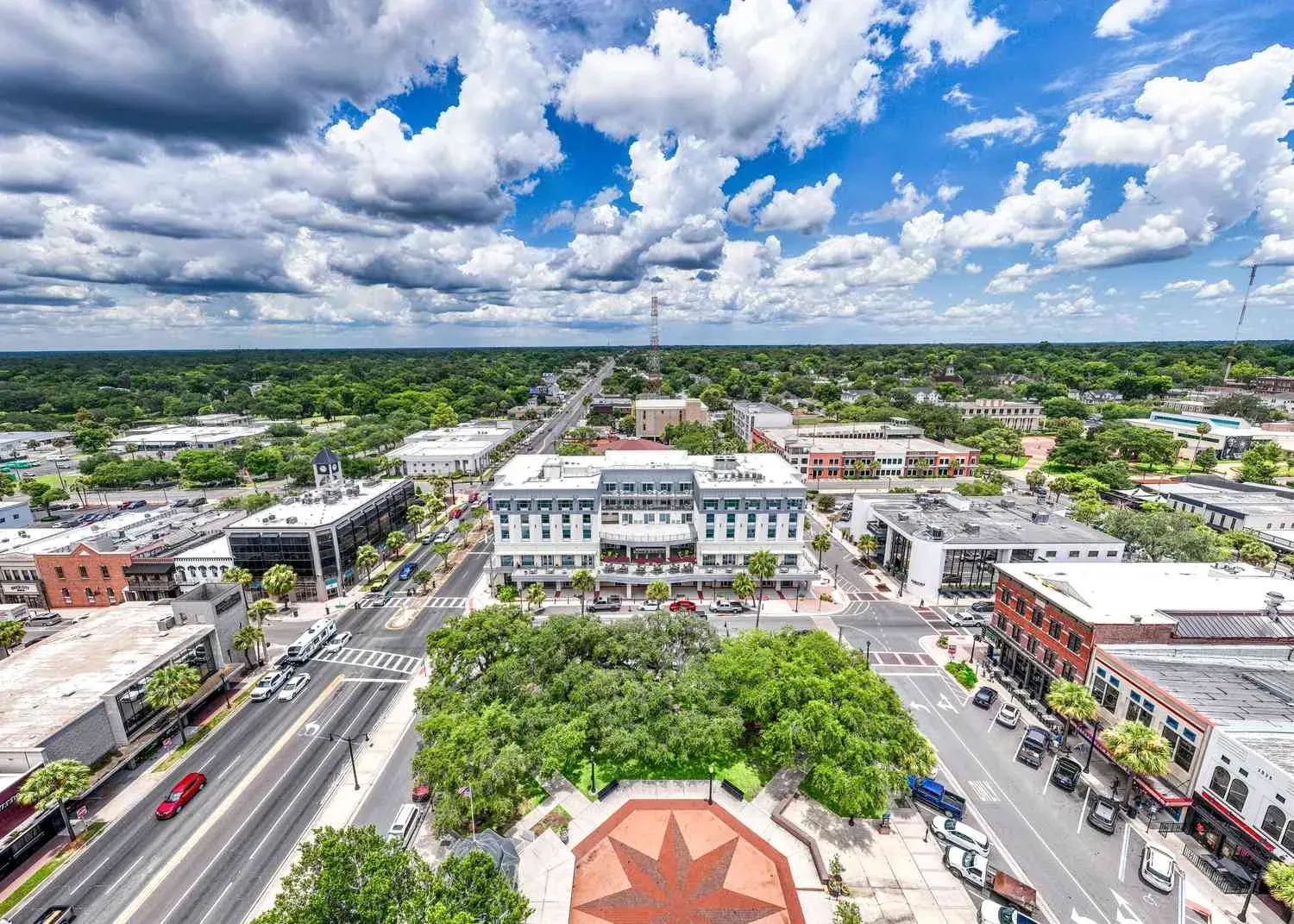 Aerial view of a small city center with streets, buildings, trees, and a bright cloudy sky