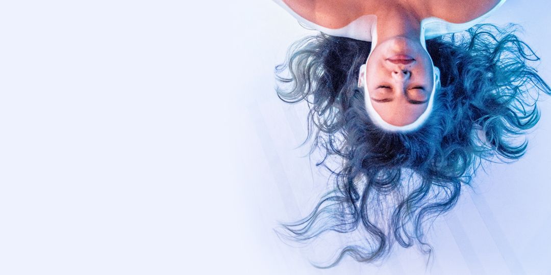 Eine Frau mit langen Haaren schwimmt mit geschlossenen Augen im blauen Wasser.