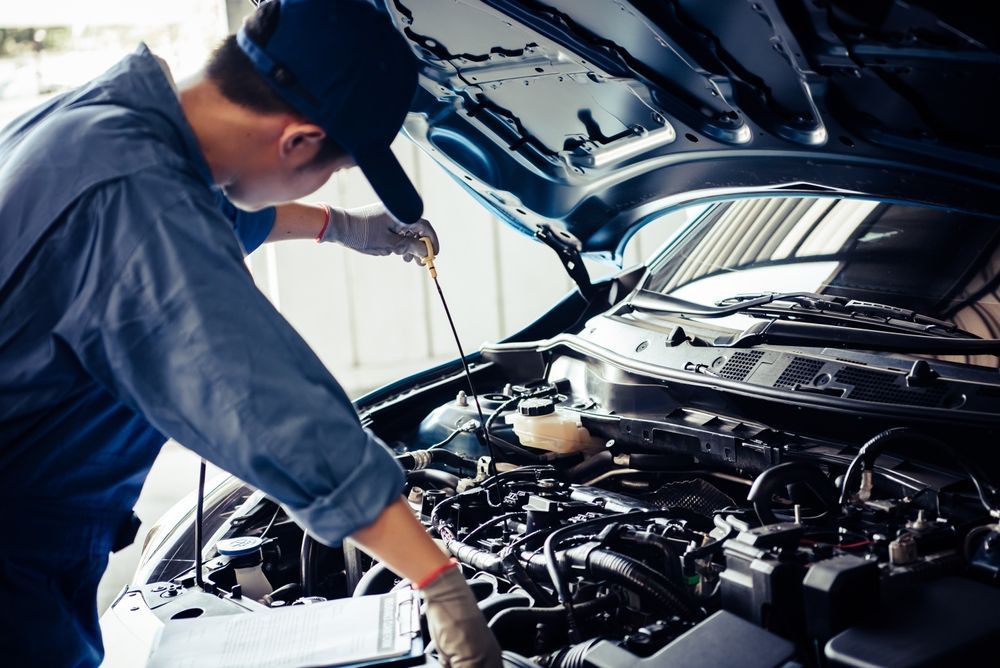 Mechanic Checking Car Engine With Dipstick, Wearing Blue Uniform and Cap — Ottos Mufflers in Noosaville, QLD