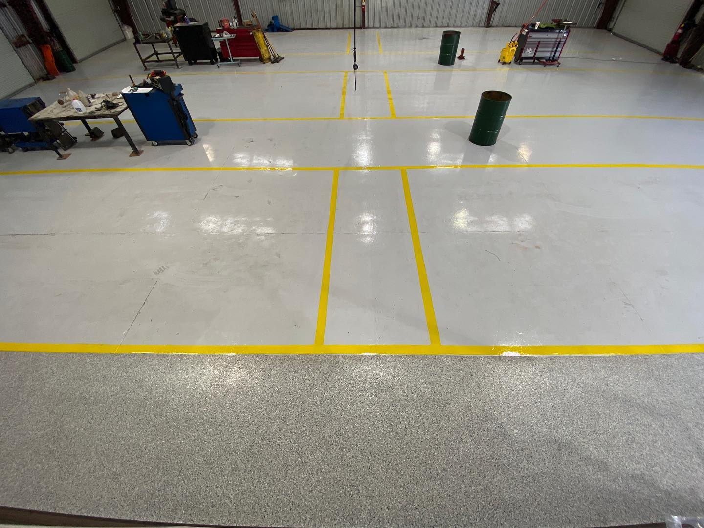 White industrial floor with yellow lines and two green barrels.