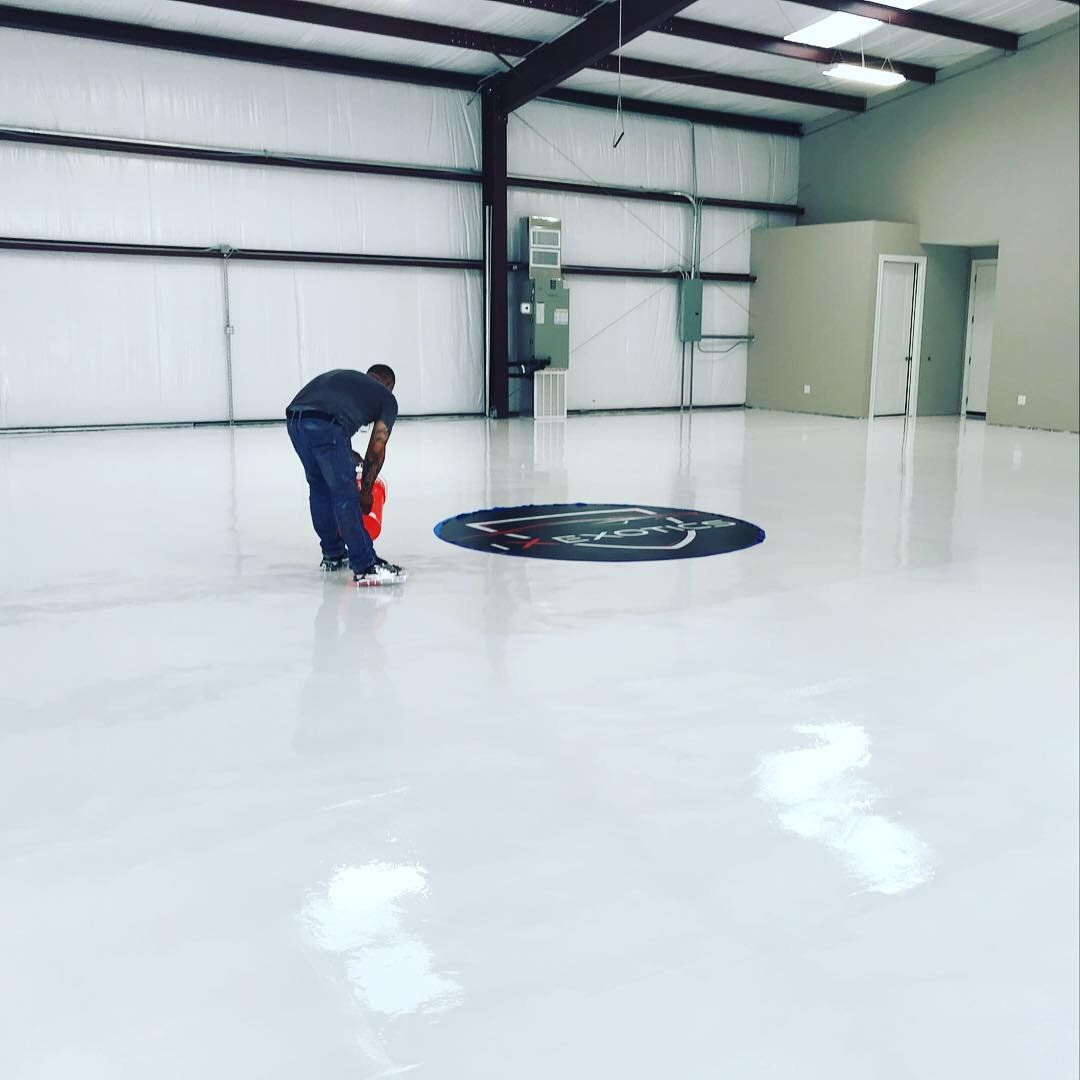 Person applying a coating to a glossy white floor in a large, empty warehouse.