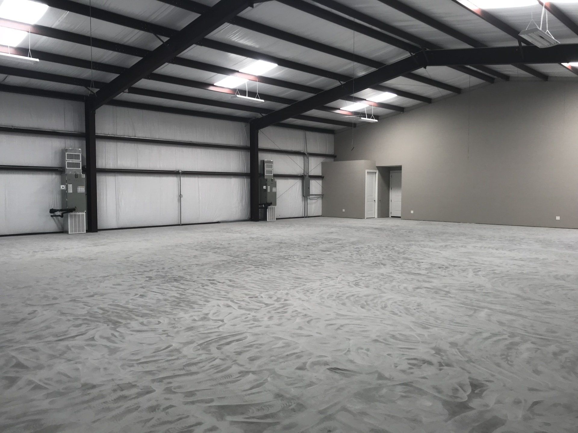 Empty, grey industrial warehouse interior with metal beams, exposed walls, and concrete floor.