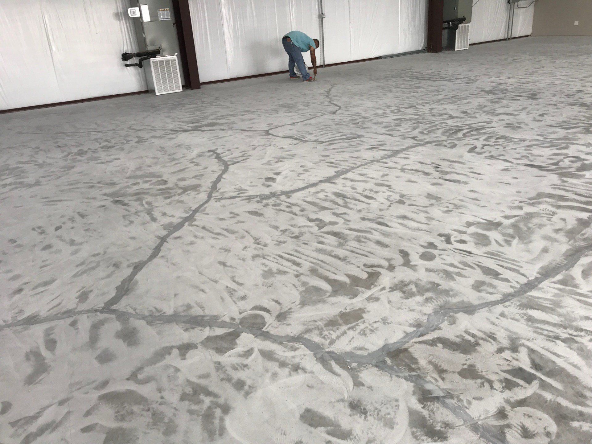 Man filling cracks in a concrete floor of a large warehouse with white walls.