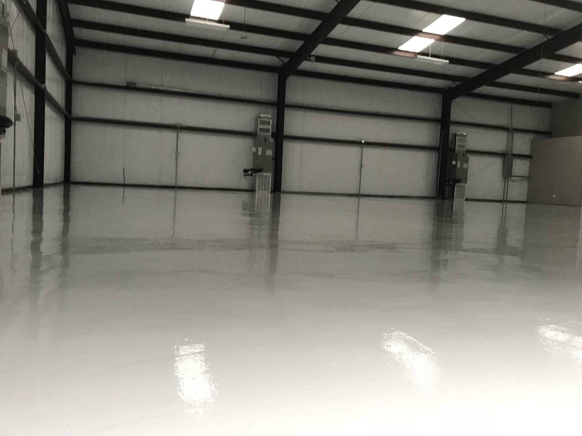 Empty warehouse with shiny, light-gray floor, metal beams, and overhead lighting.