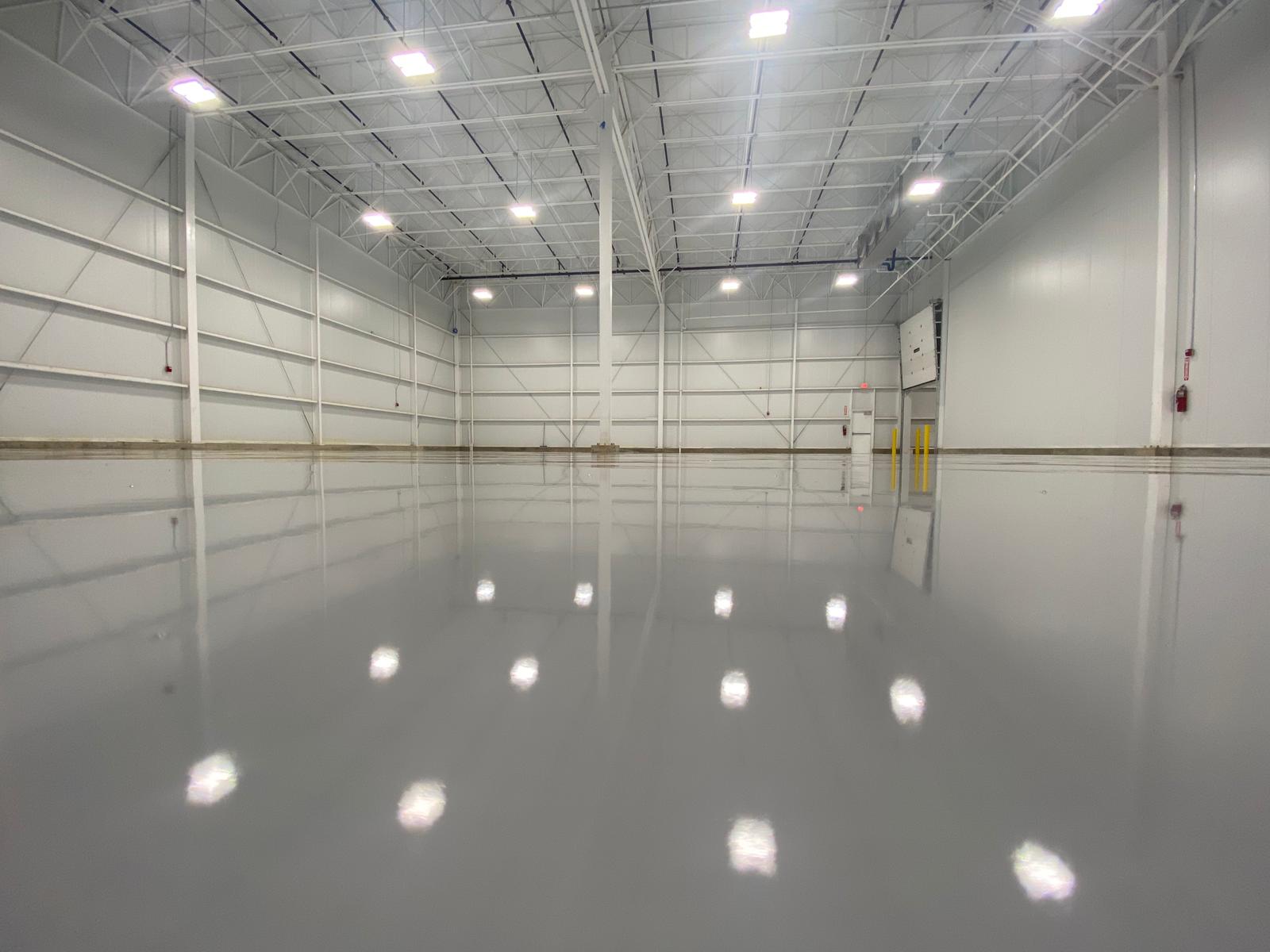 Empty, gray-floored warehouse interior with bright overhead lights reflecting in the shiny floor.