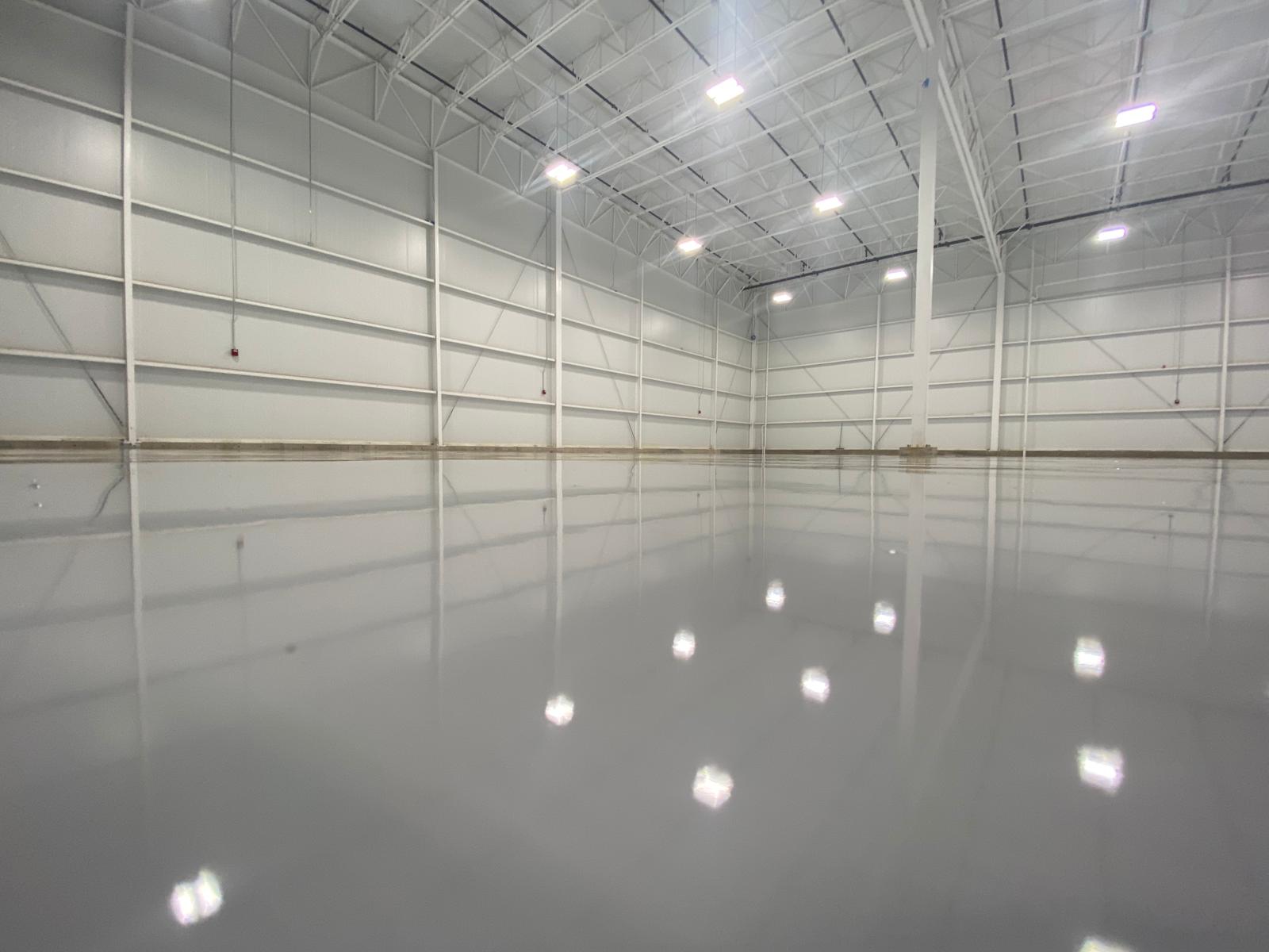 Empty, spacious industrial warehouse with a shiny gray floor and bright overhead lights.