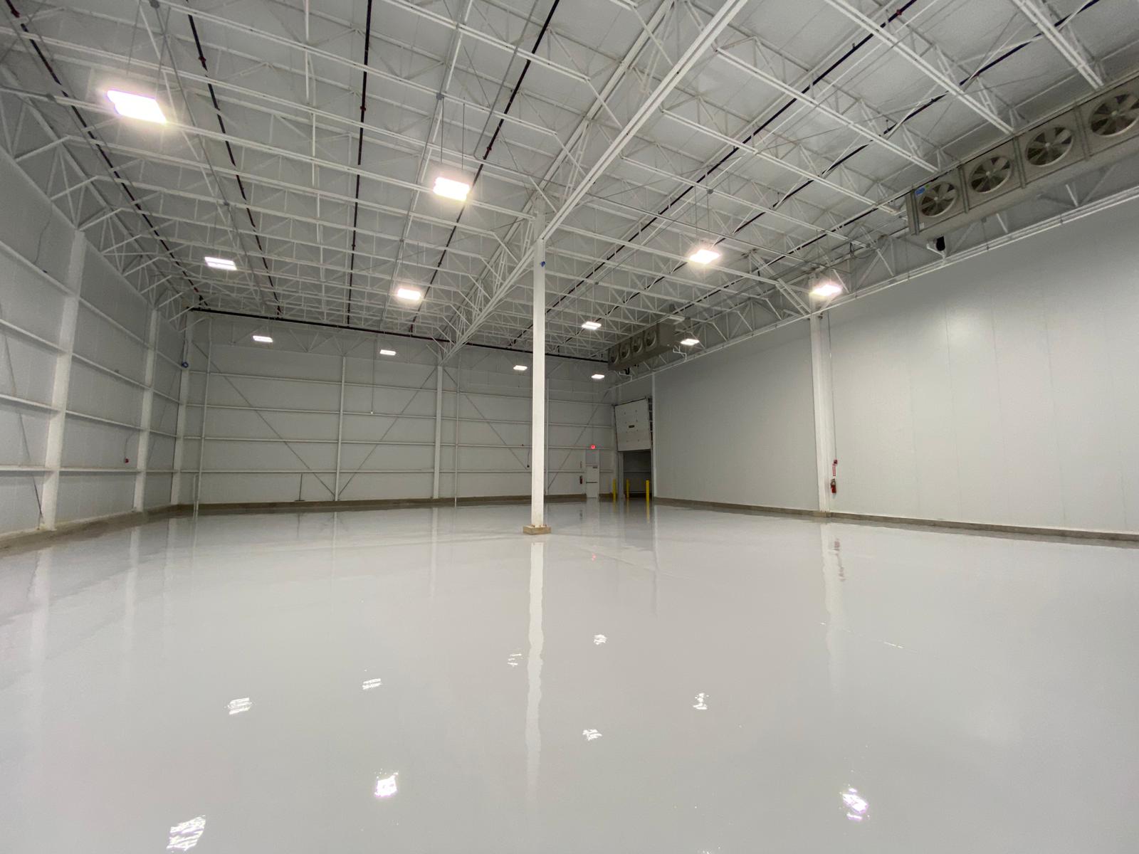 Empty, bright warehouse interior with a gray, reflective floor and white walls and ceiling.