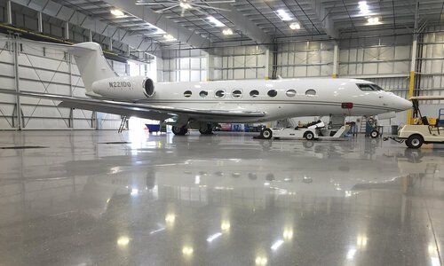 A white private jet inside a large hangar with reflective, gray flooring.