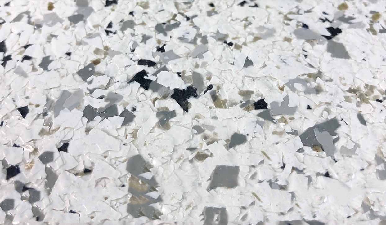 Close-up of a speckled flooring pattern with white, gray, and black chips embedded in a light-colored surface.