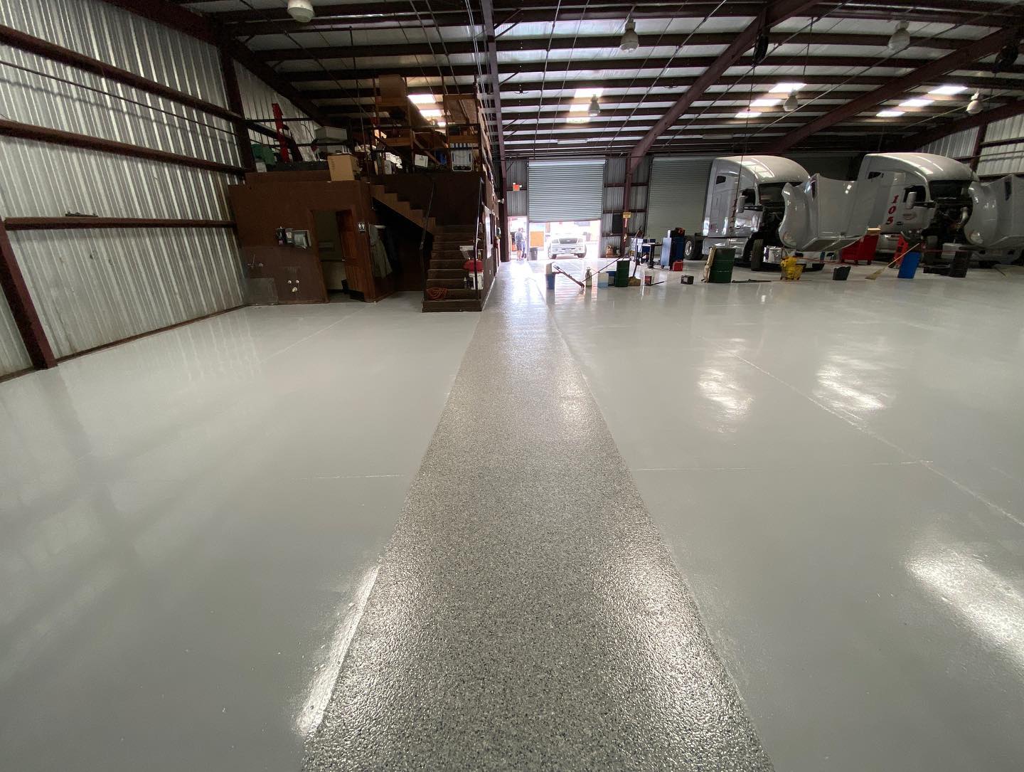 Large warehouse with reflective epoxy floor, partially speckled with aggregate, loading dock visible.