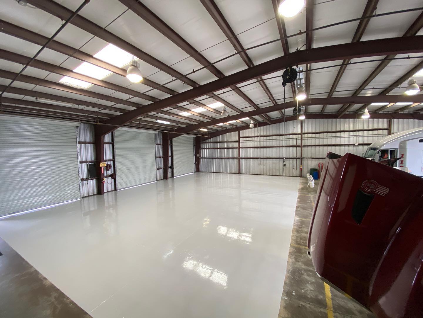 Large, empty warehouse with a shiny white floor, overhead lights, and roll-up doors.