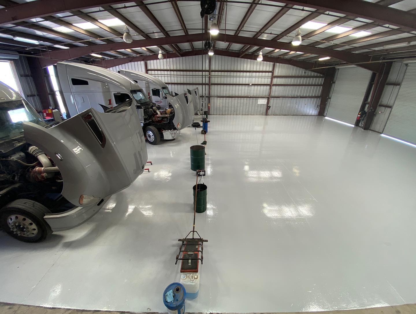 Truck repair shop with several semi-trucks being worked on; bright, clean white floor and metal structure.