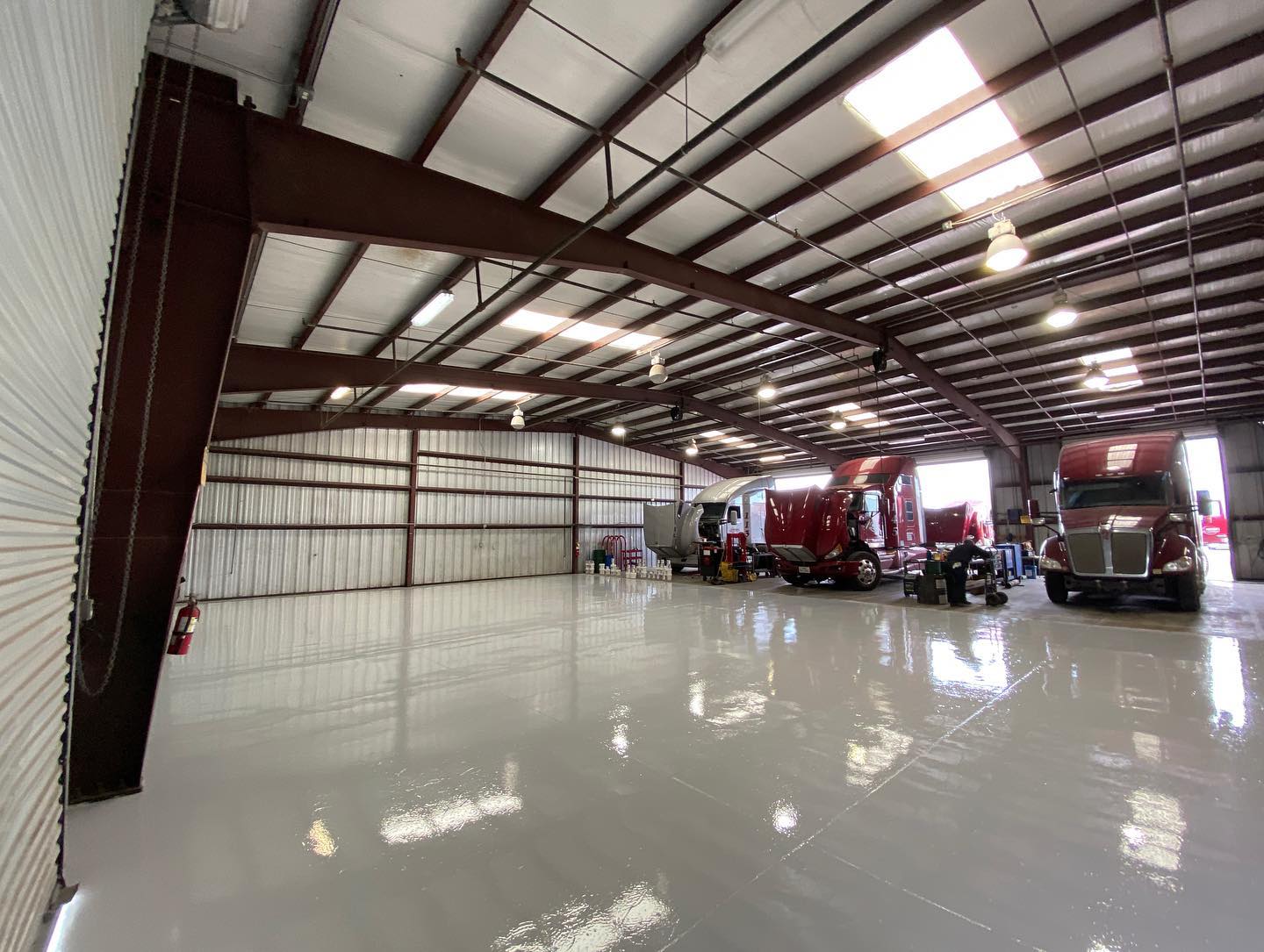 Inside a large industrial building, several red semi-trucks are parked on a glossy, light-colored floor.
