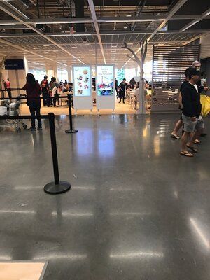 Interior view of IKEA cafeteria with people, signs, and tables. Shiny concrete floor.