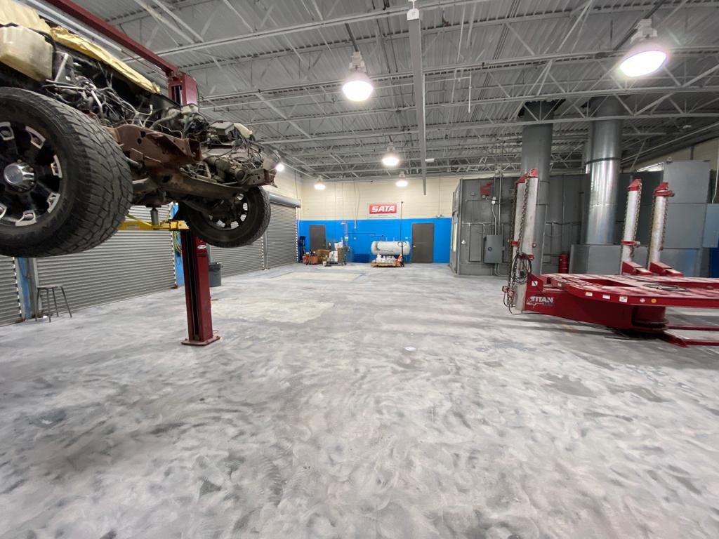 Car in auto shop lifted on a hoist. Interior shot, gray concrete floor, blue walls, bright lighting.