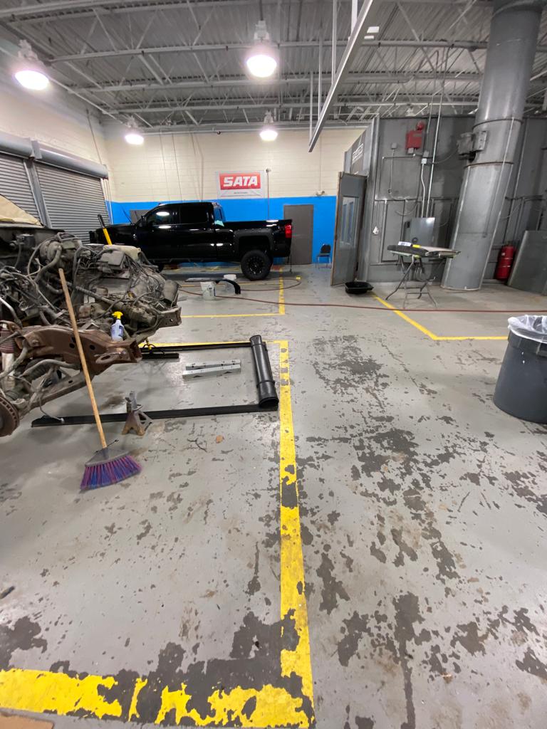 A cluttered auto body shop with a partially disassembled vehicle and a black pickup truck.