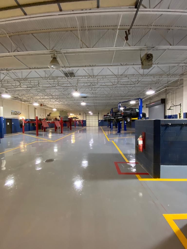 A car repair shop interior with polished gray floors, overhead lighting, and vehicles on lifts.