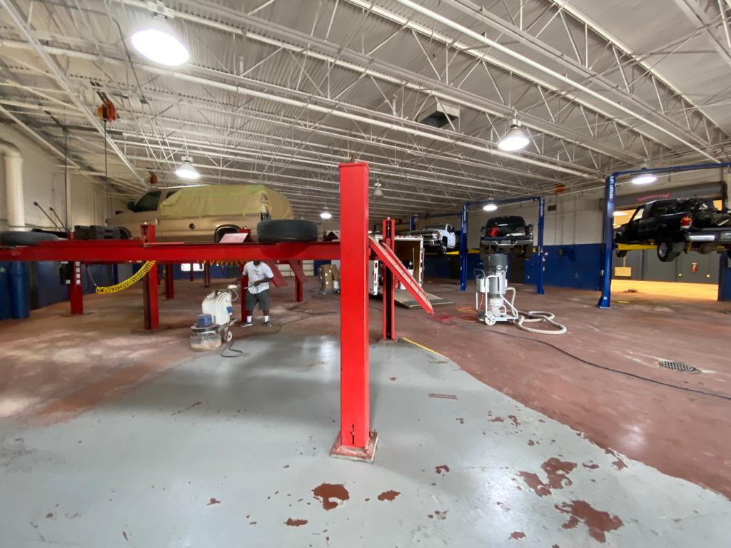 Interior of an auto repair shop with vehicles on lifts, a worker, and red and grey equipment.