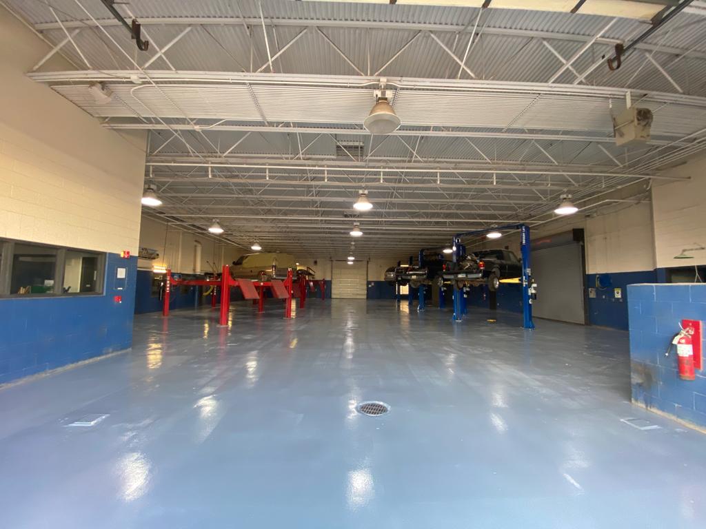 Interior of a car repair shop with several vehicles on lifts. Blue and white walls, grey floor.
