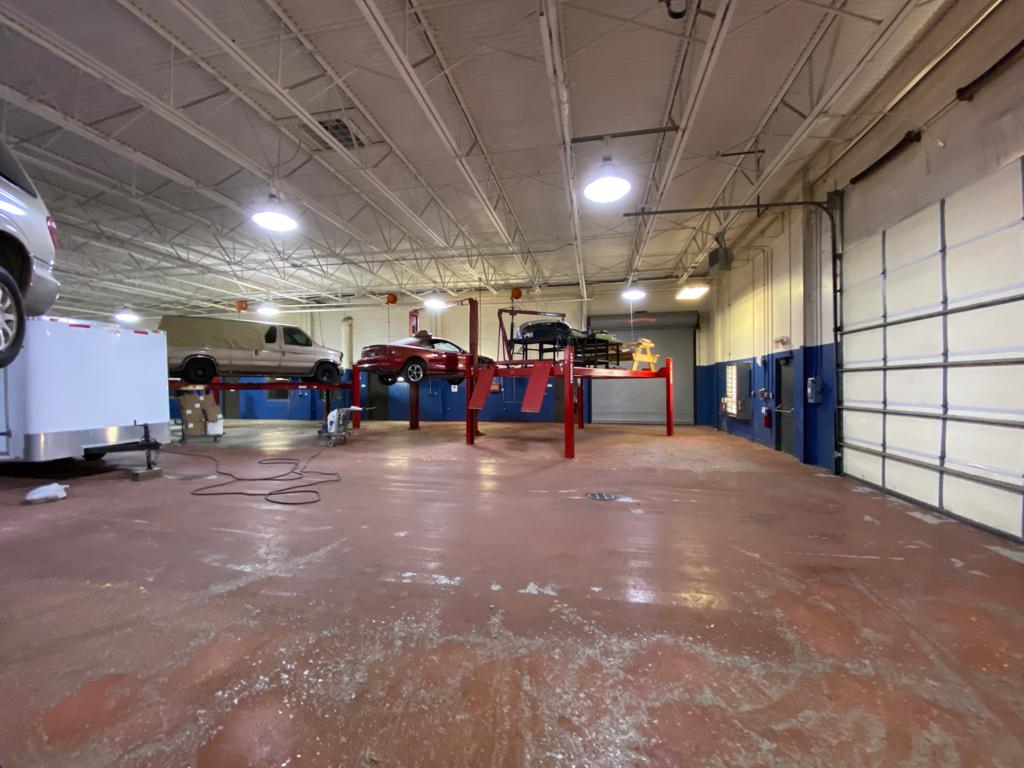 An auto repair shop interior with several vehicles on lifts. The floor is red, and a garage door is visible.