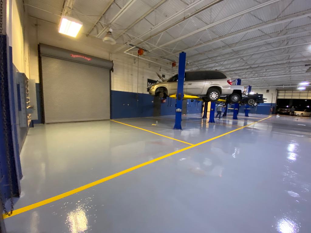 Car in auto repair shop, lifted on a blue hydraulic lift. Light gray floor with yellow lines, blue walls.