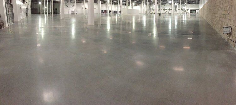 An empty, spacious warehouse with a polished concrete floor reflects overhead lights.