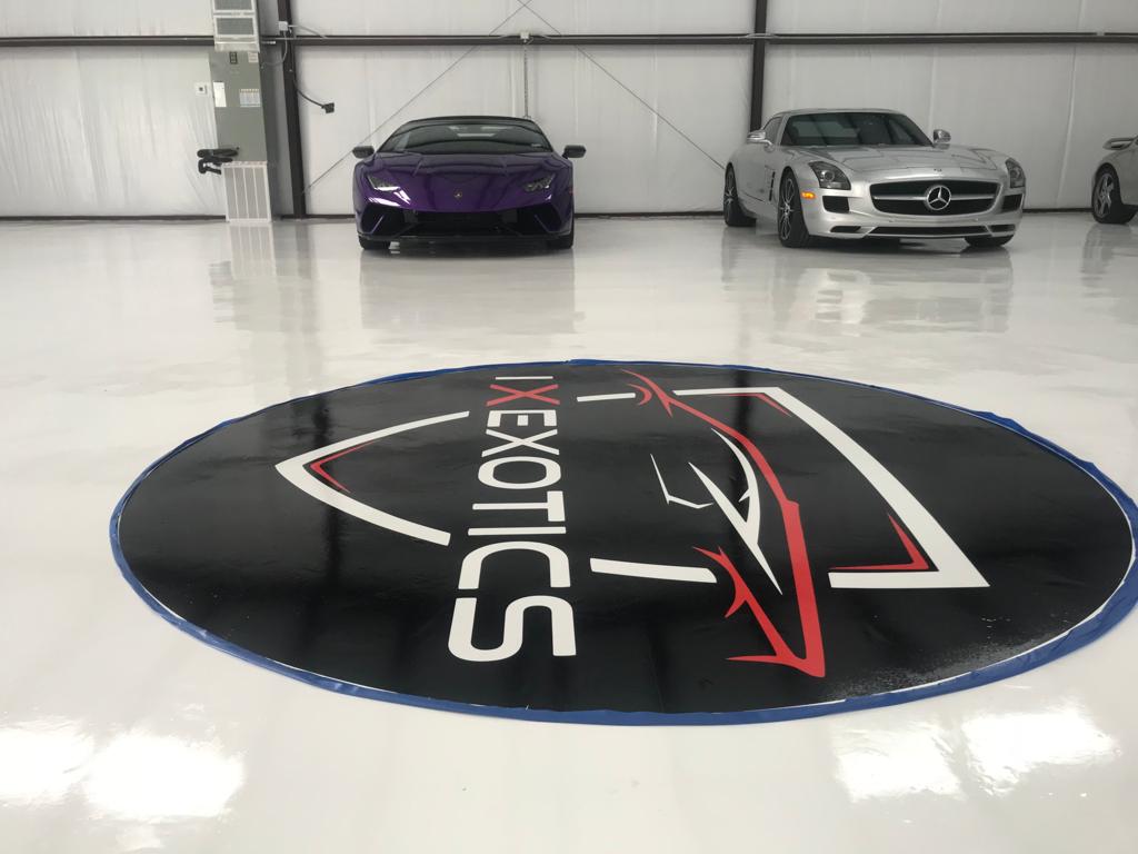 Interior of a garage with a logo on the floor and two luxury cars.