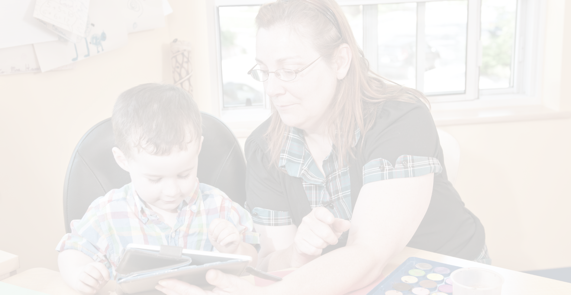 A woman and a child are sitting at a table looking at a tablet.