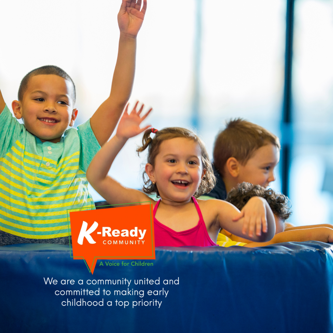 A group of children are sitting in front of a sign that says k-ready