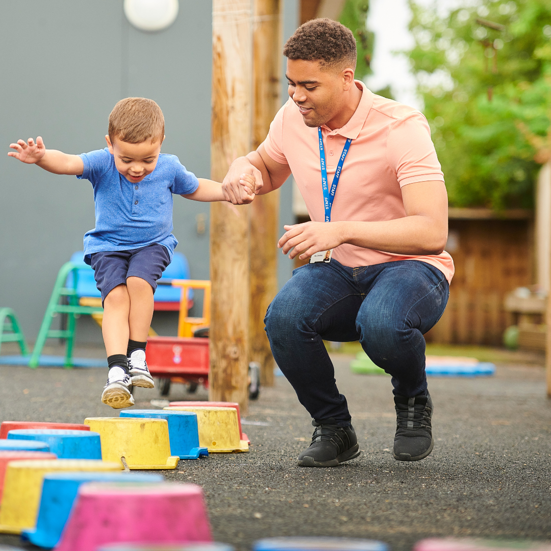 A man is kneeling down next to a young boy who is jumping in the air.