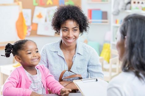 A woman and a little girl are sitting at a table talking to a doctor.