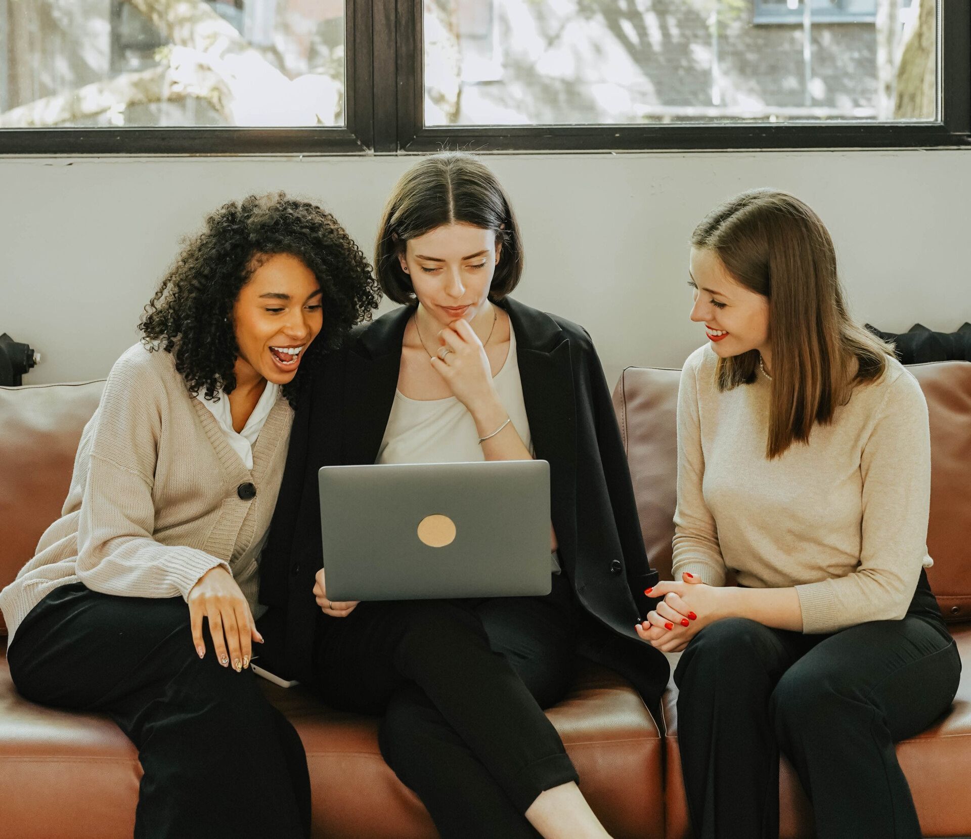 Three women are sitting on a couch looking at a laptop.