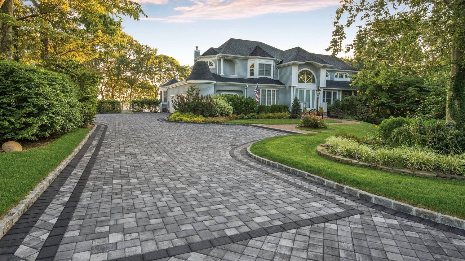 Beige stone walkway leading to a red double door entrance, surrounded by plants and mulch.