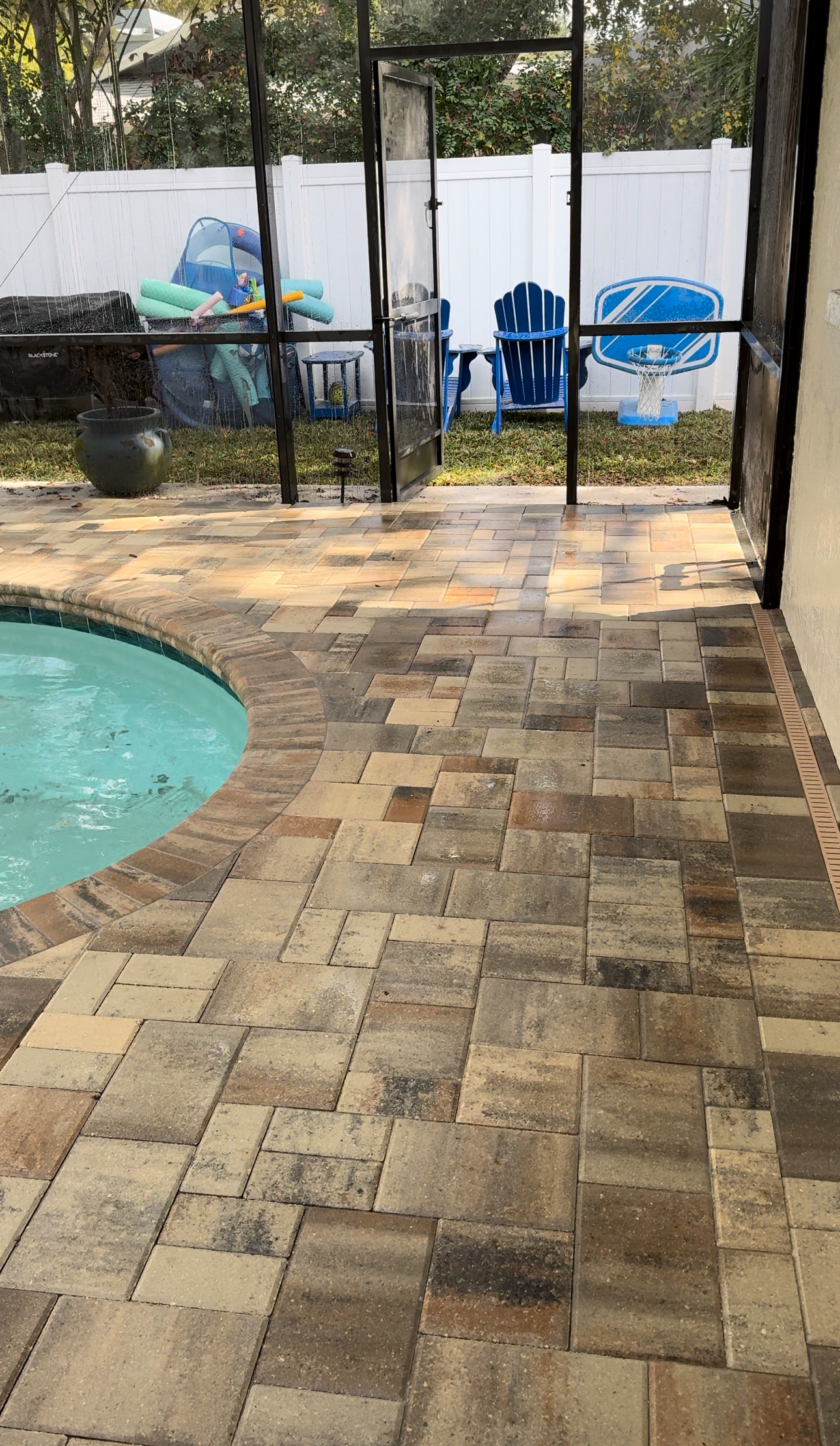 Brick paved driveway leading to a white, open-air carport with green landscaping on the right.