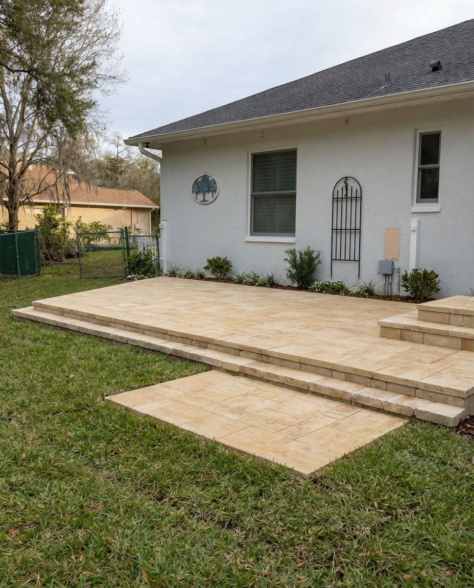 Backyard patio with light tan pavers, steps, and house with blue and green decorations.