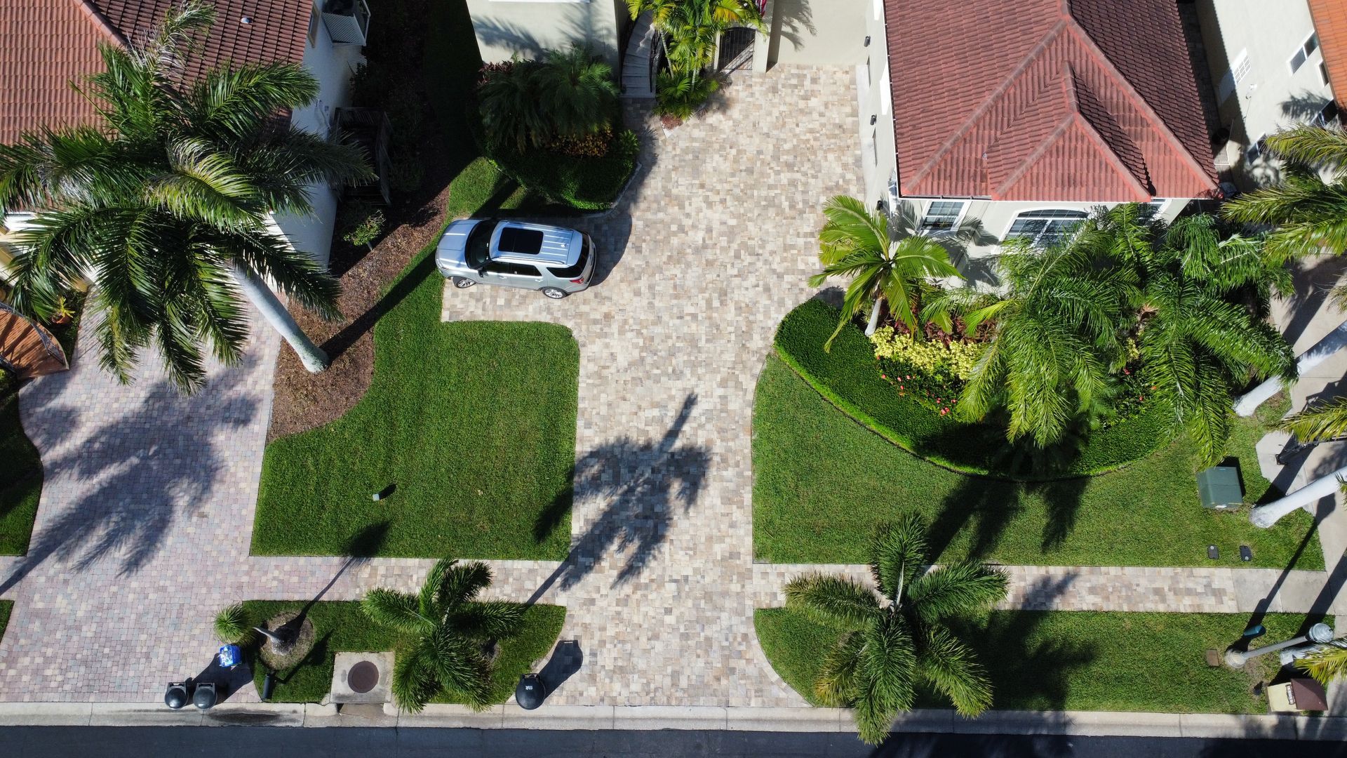 Stone paver driveway leading to a two-car garage with brown doors, bordered by green grass and a street curb.
