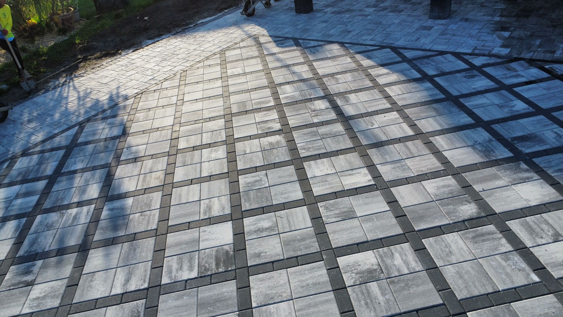 Gray brick patio with dark gray grid pattern; sunlight casts shadows.