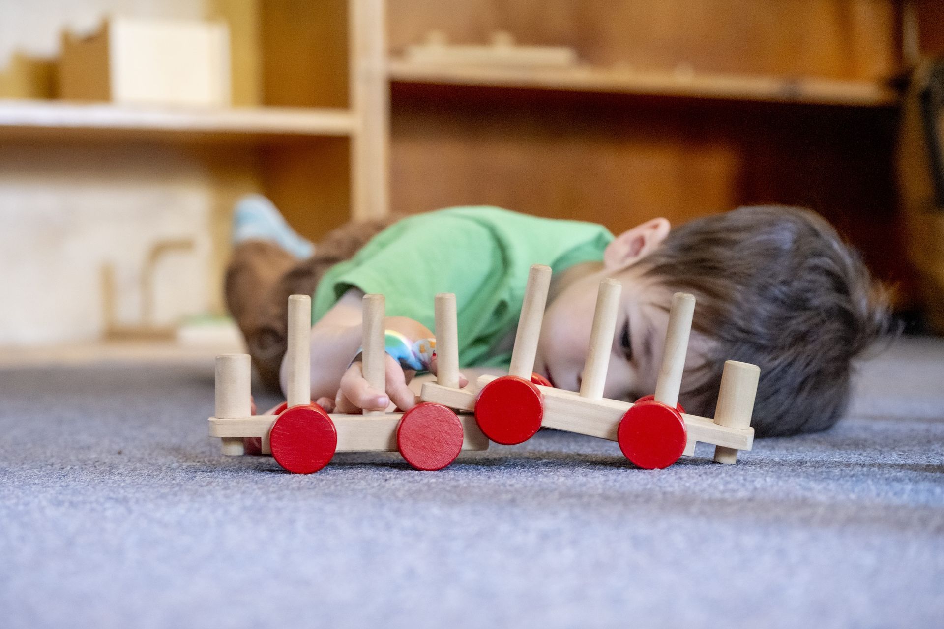 Montessori child is laying on the floor working with a wooden toy train.
