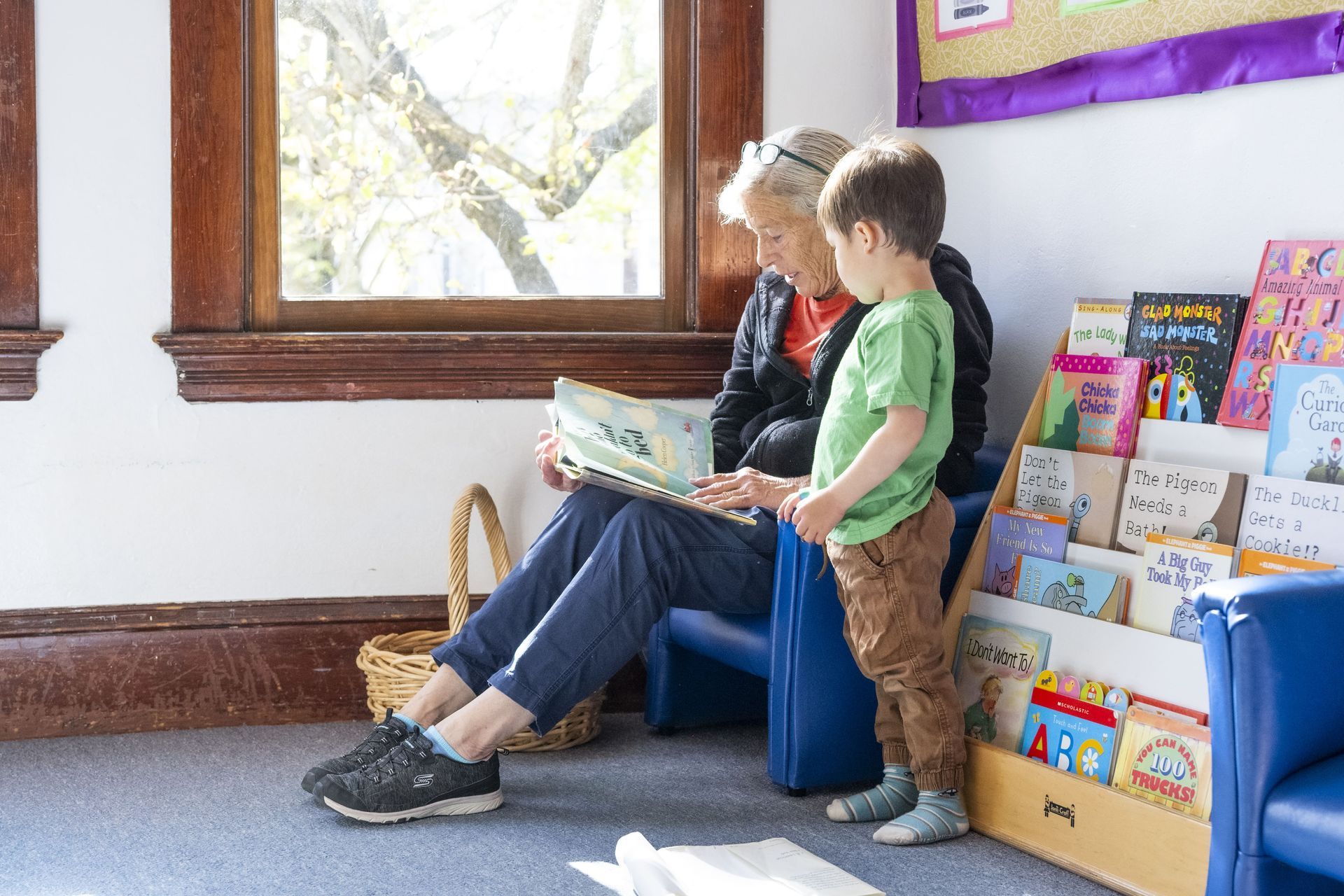 A Montessori guide and a child are sitting in a waiting room reading books.