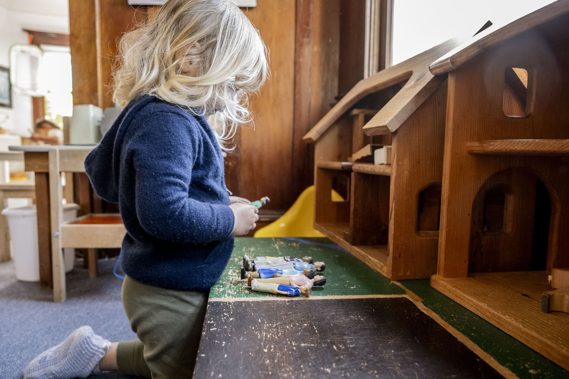A Montessori children is playing with a wooden doll house.