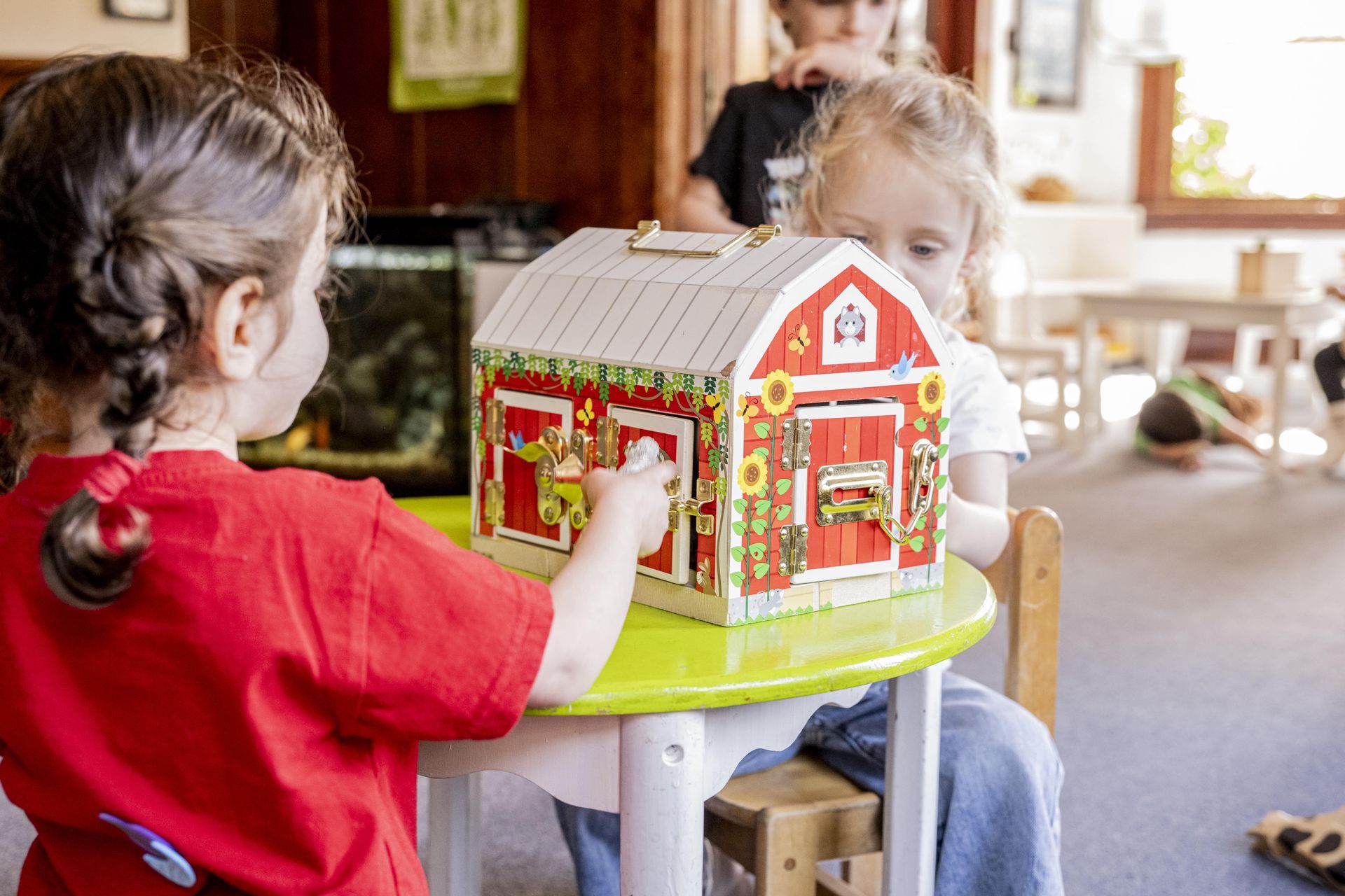 A Montessori childr is sitting at a table working with a toy barn.