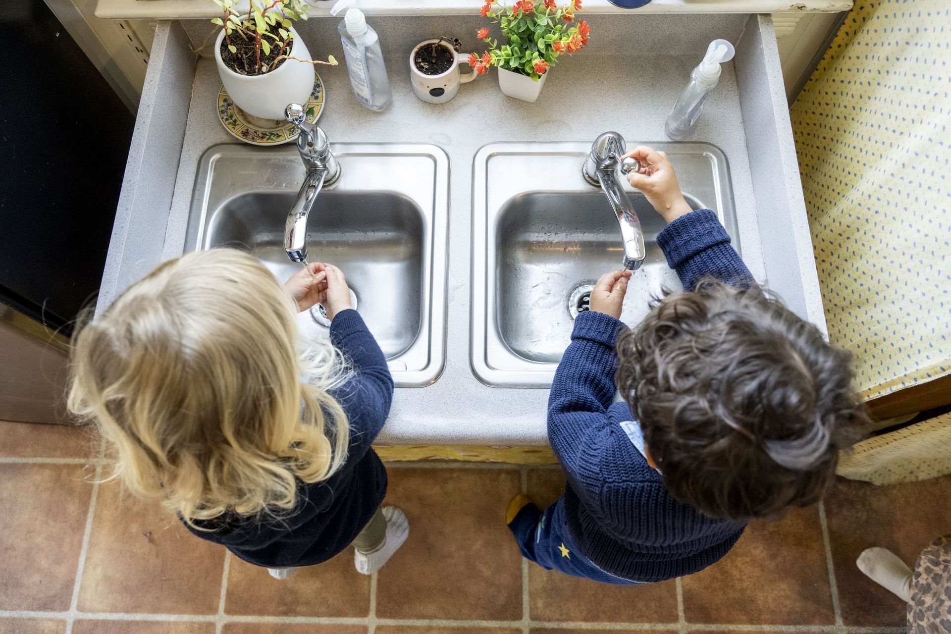 Montessori children are washing dishes in a kitchen sink.
