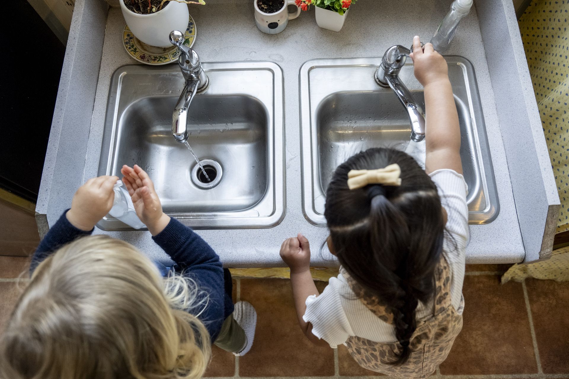 Montessori children are washing dishes in a kitchen sink