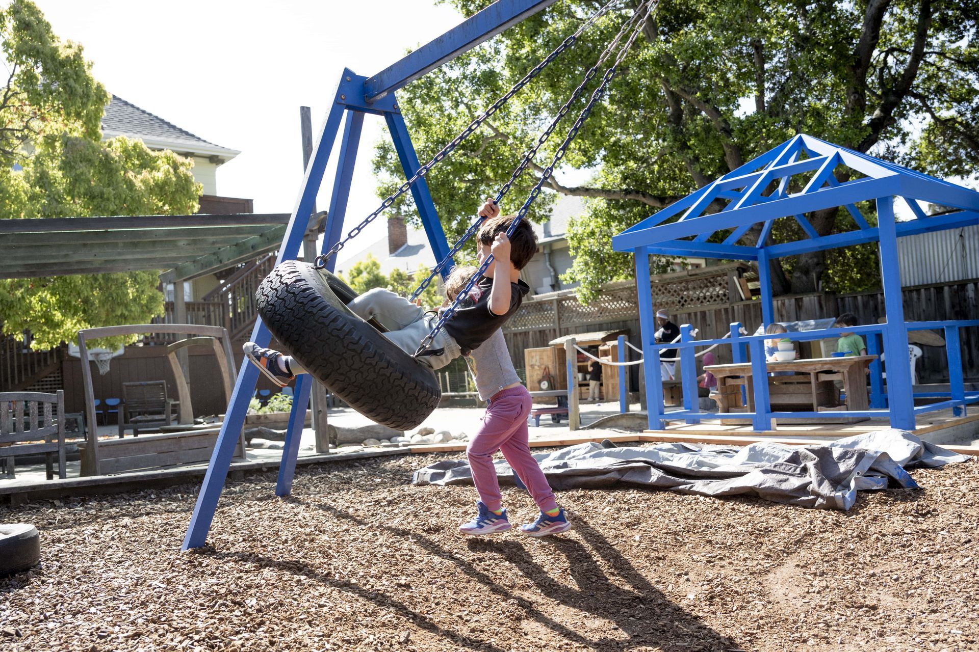 Two Montessori children are playing on a tire swing in a playground.